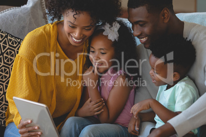 Happy African American parents with their cute children using digital tablet on sofa