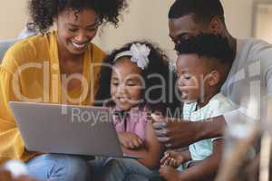 Happy African American parents with their cute children using laptop on sofa