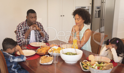 African American family with hands clasped and eyes closed praying together at dining table
