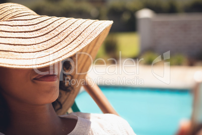 African American woman with hat relaxing on sun lounger in her backyard