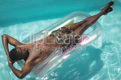 Young African American man with hands behind head relaxing on pool lounger