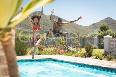 Happy young African American couple jumping in a swimming pool in their backyard