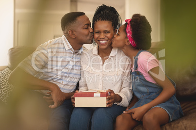 Happy African American father and daughter kissing mother on cheeks