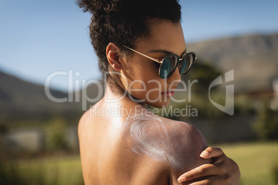 Young mixed-race woman rubbing sunscreen on shoulders