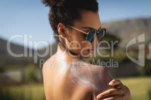 Young mixed-race woman rubbing sunscreen on shoulders
