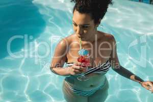 Young mixed-race woman drinking cocktail in swimming pool