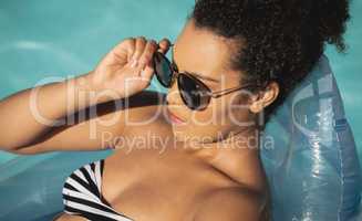 Young mixed-race woman with sunglasses relaxing on pool inflatable