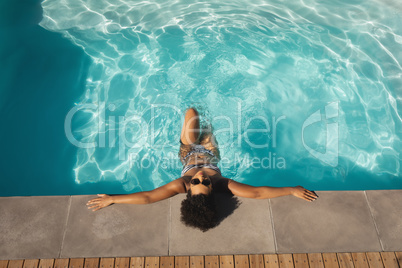 Young mixed-race woman with sunglasses leaning on edge of pool