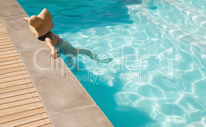 Young mixed-race woman with hat leaning on edge of pool