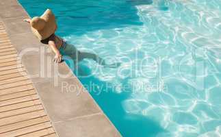Young mixed-race woman with hat leaning on edge of pool