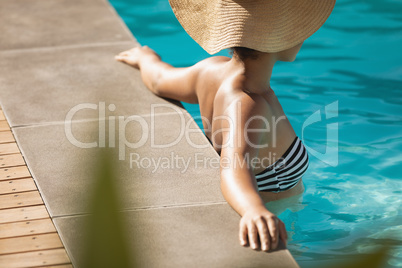 Young mixed-race woman with hat leaning on edge of pool