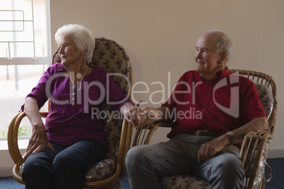 Front view of senior couple holding hands and looking away at nursing home