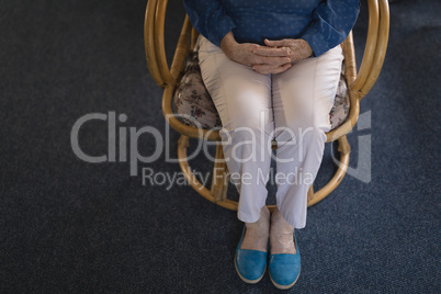 Low section of senior woman with hand clasped sitting on chair