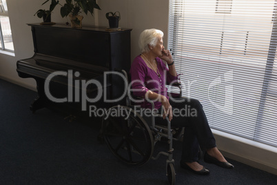 Side view of disabled senior woman sitting on wheelchair and looking outside through window