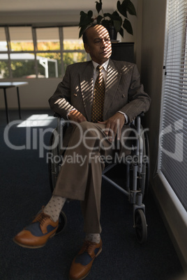 Front view of disabled senior man sitting on wheelchair and looking outside through window