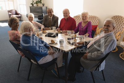 Front view of happy group of senior friends sitting on dining table and looking at camera