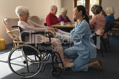 Side view of female doctor holding hands and talking with disable senior woman at home