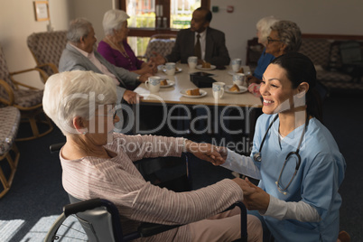 Side view of female doctor holding hands and talking with disable senior woman at nursing home