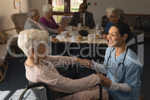 Side view of female doctor holding hands and talking with disable senior woman at nursing home