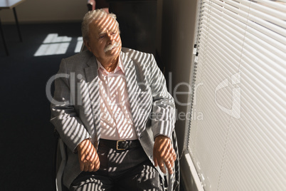 Front view of disable senior man sitting on wheelchair and looking outside through window
