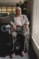 Front view of disable senior man sitting on wheelchair and looking outside through window
