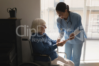 Female doctor discussing medical report with disable senior woman on digital tablet