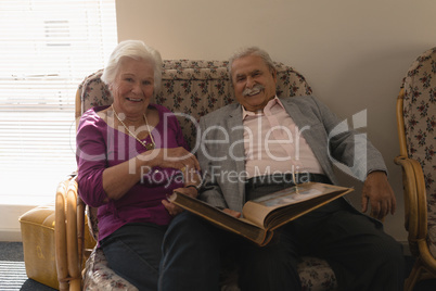 Front view of senior couple with photo album looking at camera in home