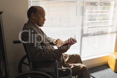 Side view of disable senior man sitting on wheelchair and reading a book