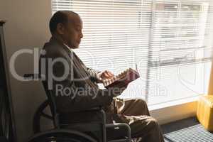 Side view of disable senior man sitting on wheelchair and reading a book