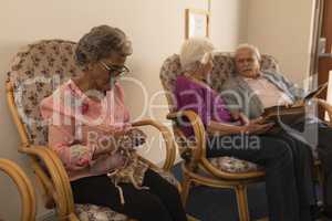 Senior friends knitting and looking photo album at nursing home