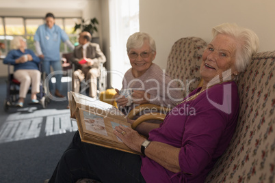 Side view of senior women with photo album looking at camera in home