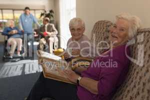 Side view of senior women with photo album looking at camera in home