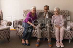 Front view of senior friends using laptop while sitting on sofa