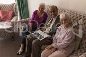 Senior friends with laptop sitting on sofa and looking at camera