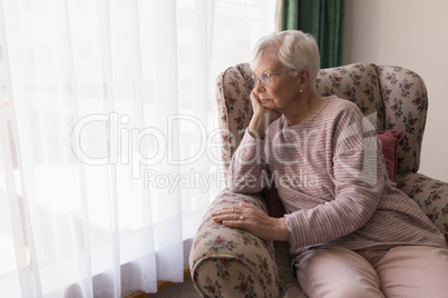 Front view of senior woman sitting on the couch and looking outside through window