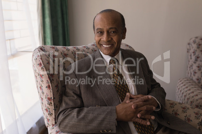 Front view of senior man with hand clasped looking at camera in home