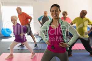 Front view of happy female trainer looking at camera while assisting senior people