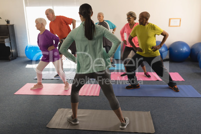 Rear view of female trainer assisting senior people in fitness studio