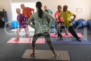 Rear view of female trainer assisting senior people in fitness studio