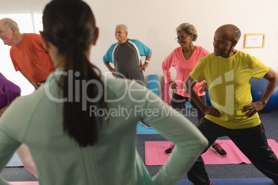 Rear view of female trainer assisting senior people in fitness studio