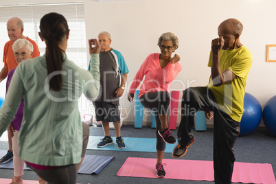 Rear view of female trainer assisting senior people in fitness studio