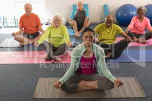 Senior people doing yoga with female trainer in fitness studio