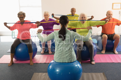 Young female trainer and senior people exercising with resistance band