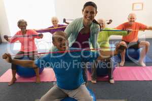 Young female trainer assisting senior man in fitness studio