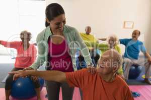 Young female trainer assisting senior man in fitness studio