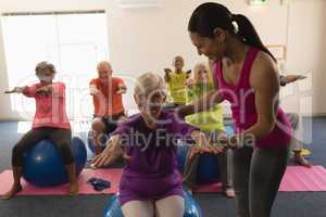 Young female trainer assisting senior woman in fitness studio