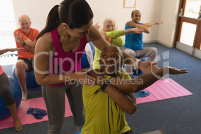 Young female trainer assisting senior man in fitness studio