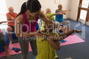 Young female trainer assisting senior man in fitness studio