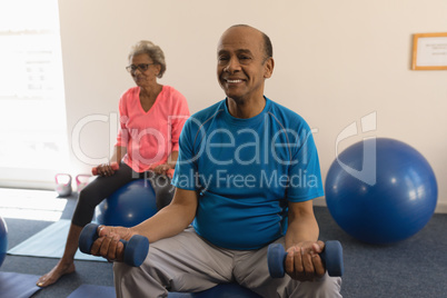 Front view of senior man exercising with dumbbells in fitness studio