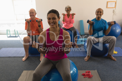 Front view of senior people exercising with female trainer using dumbbells